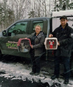 Two people holding pet carriers in front of a SPCA truck