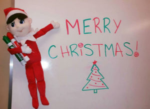 Eddie the Elf beside a whiteboard that says Merry Christmas